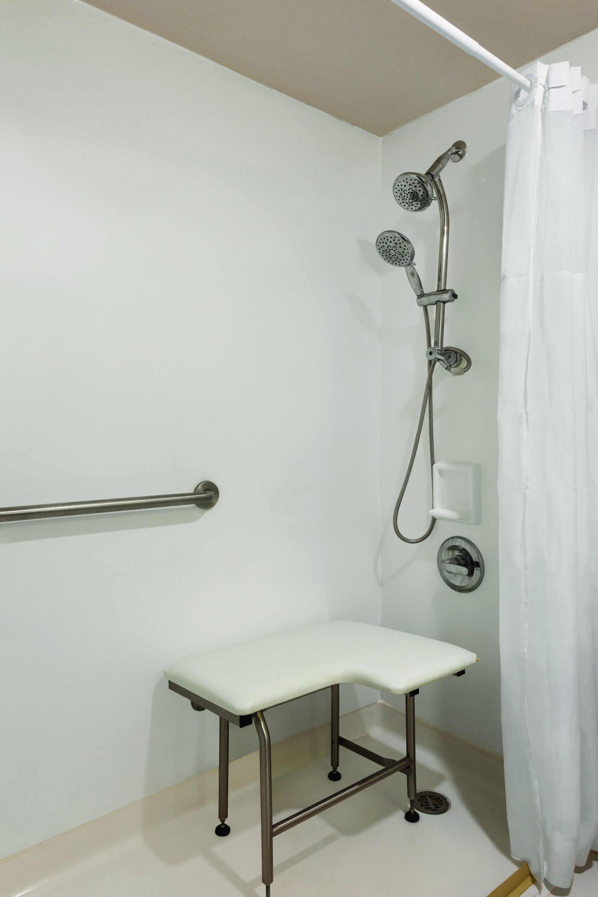 Un espace douche équipé d’un pommeau de douche à main, d’un panneau de commande de douche et d’un rideau de douche blanc.