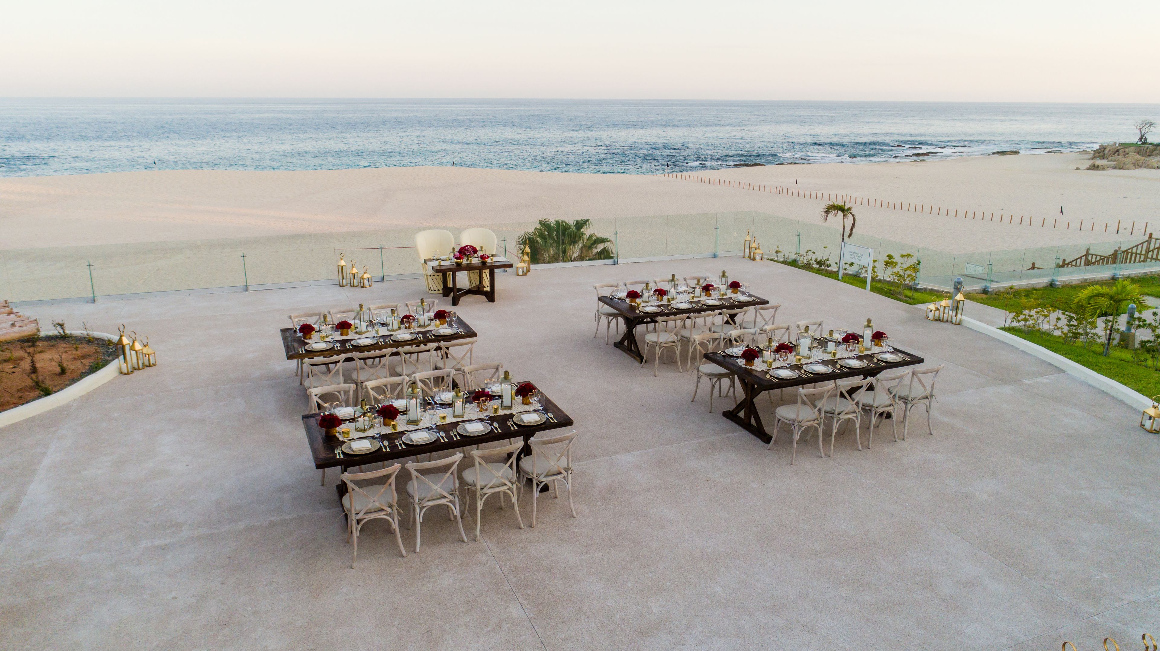 Un espace de restauration en plein air, avec des tables dressées pour le repas, offrant une vue sur une plage et l’océan.