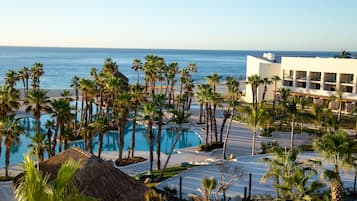 A resort with a swimming pool, palm trees, and a view of the ocean.