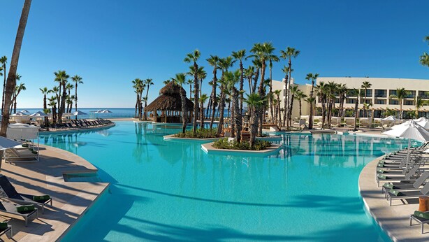 A resort pool with palm trees, lounge chairs, and a building in the background. - Paradisus Los Cabos – Adults Only – All Inclusive – The Leading Hotels of the World (San José del Cabo)