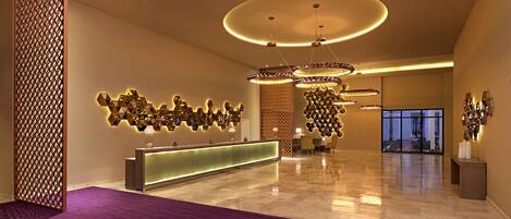 A modern lobby with a reception desk, decorative wall art, and a large chandelier.