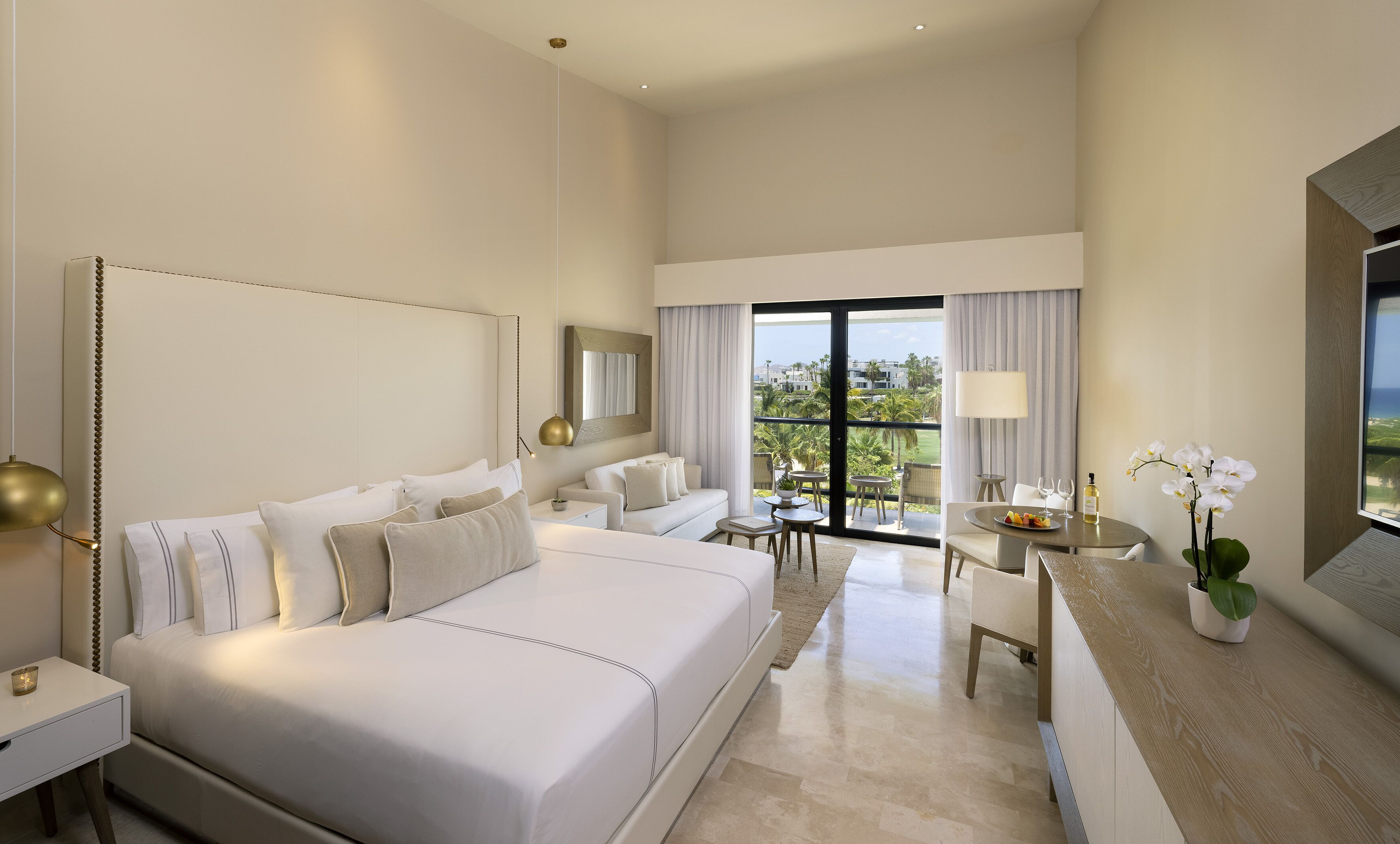 A hotel room with a large bed, a desk with a chair, a dining table with chairs, and a balcony with a view.