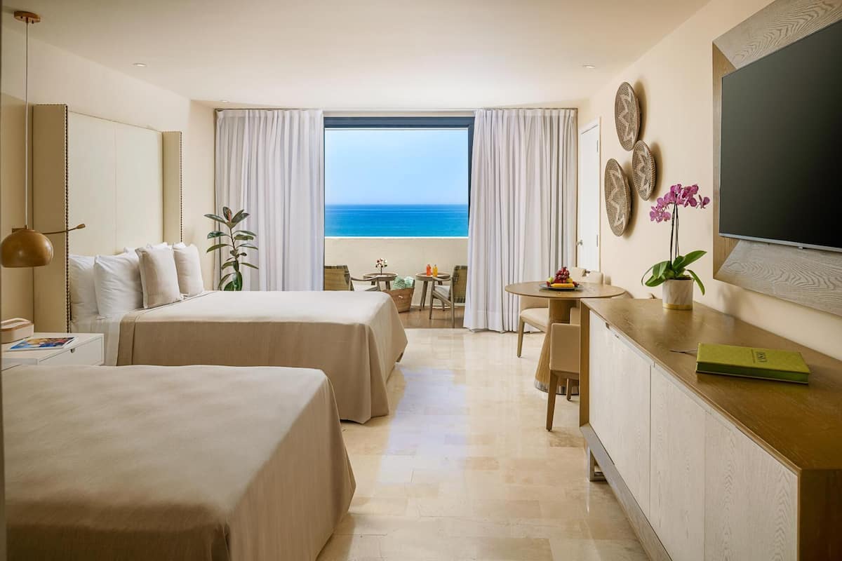 Ein Hotelzimmer mit zwei Betten, einer Essecke, einem Fernseher und Meerblick.