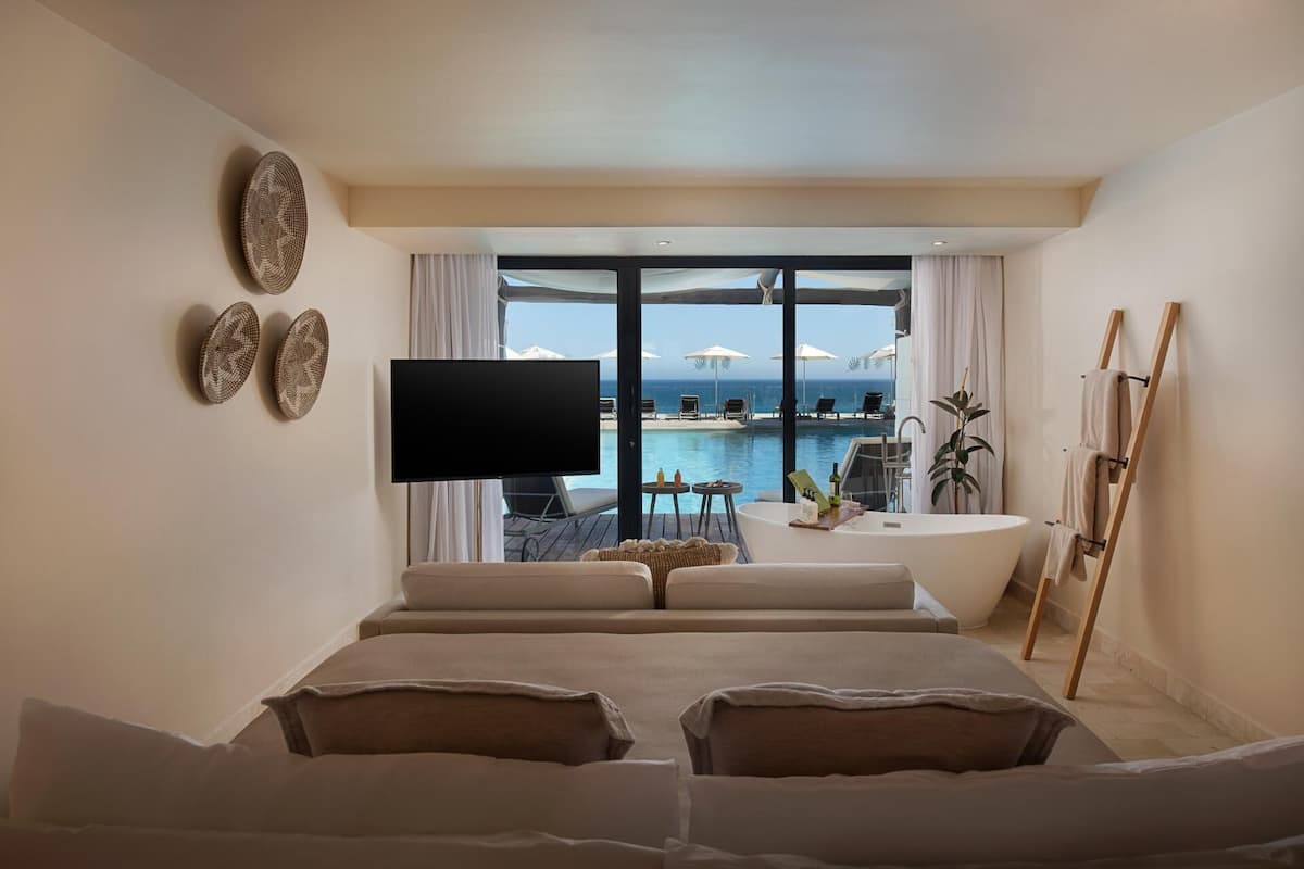 Ein modernes Hotelzimmer mit einem großen Bett, einem Flachbildfernseher, Blick auf den Ozean und einem Poolbereich.