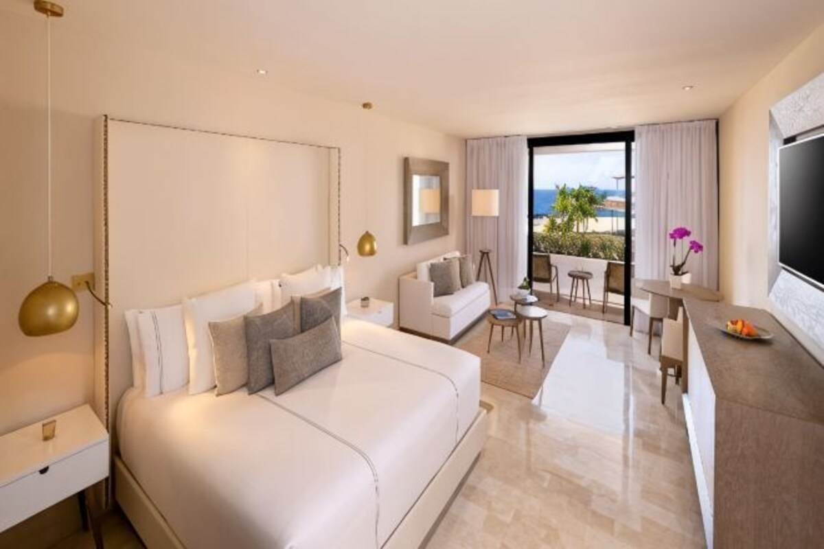 A hotel room with a large bed, a desk, a sofa, and a balcony with a view.