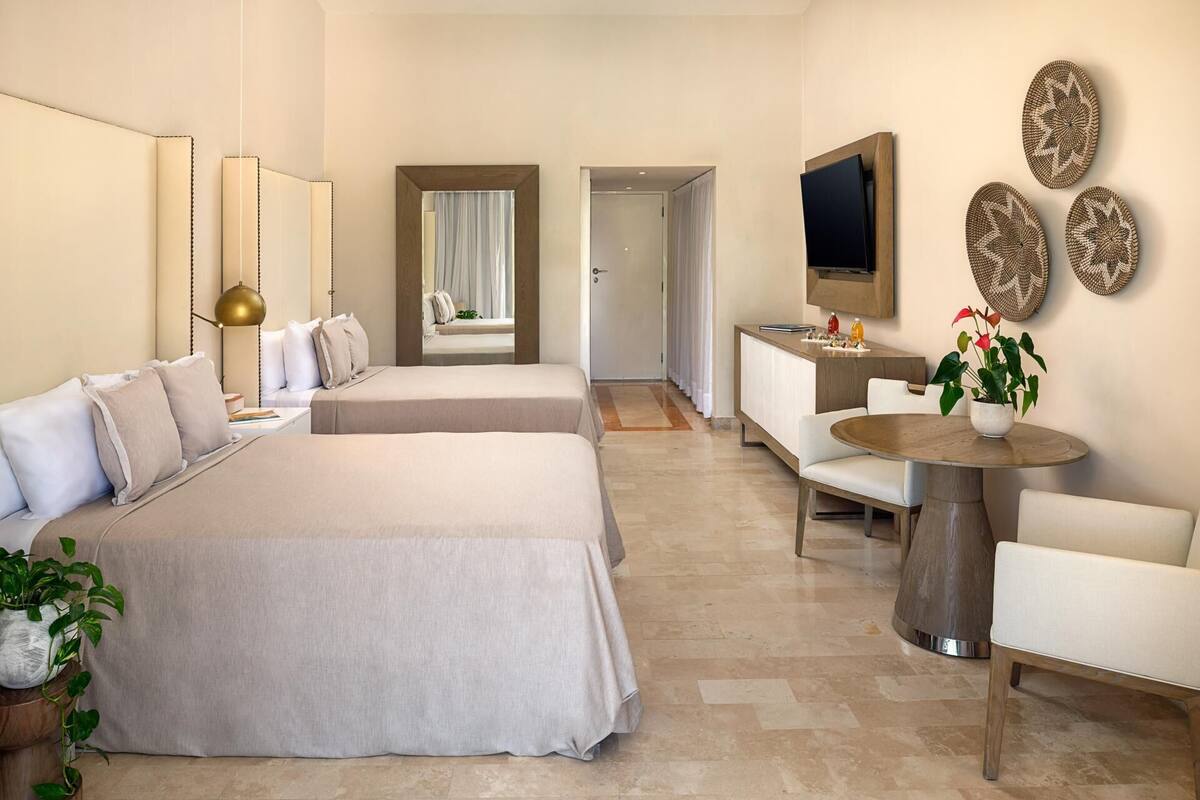 Ein Hotelzimmer mit zwei Betten, einem Fernseher, einem Essbereich mit Tisch und Stühlen sowie Wanddekoration.