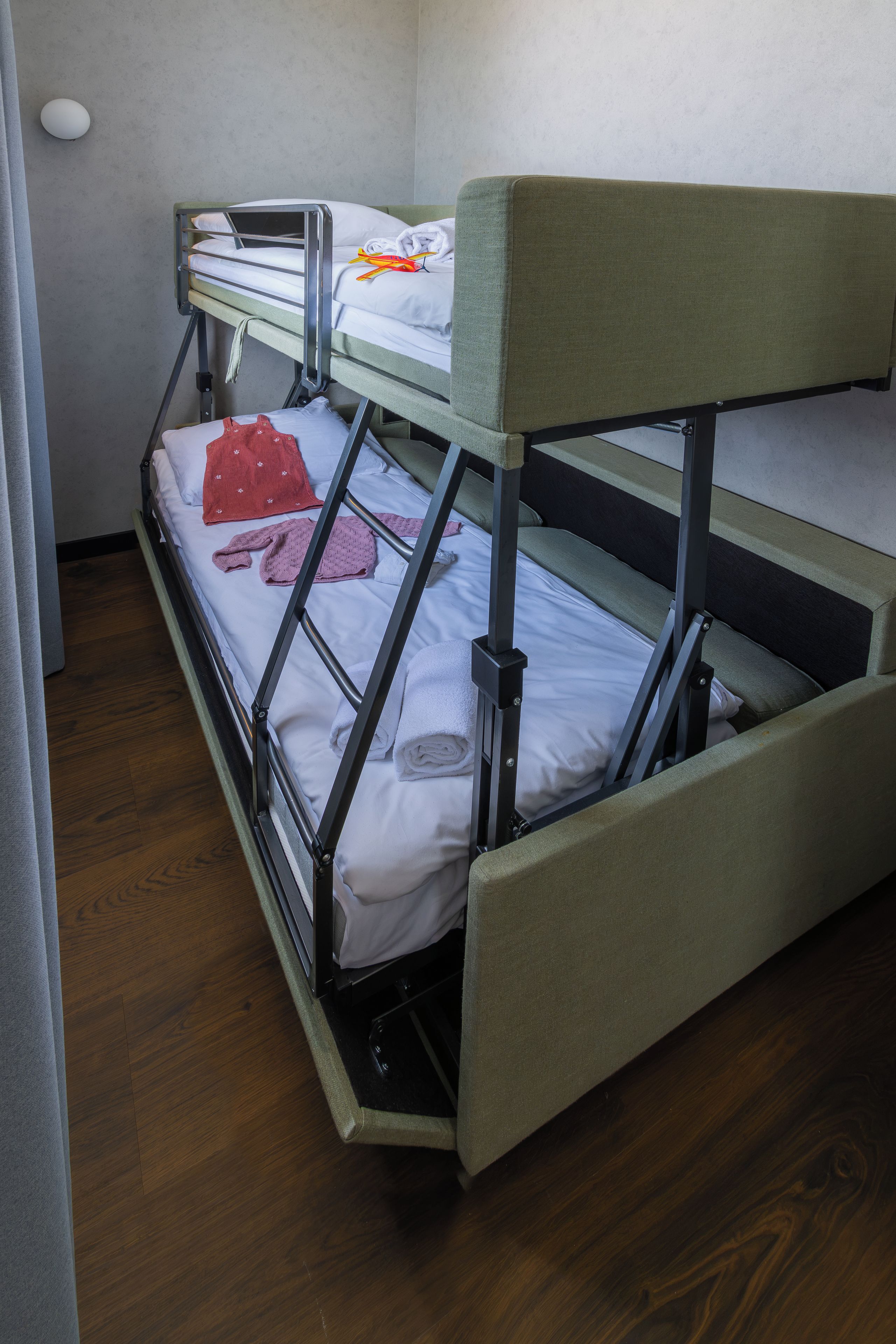 Ein Etagenbett mit ausziehbaren Bettkasten, einem weißen Kopfkissen, einem roten Handtuch und einem Paar rosafarbener Socken auf dem unteren Bett.