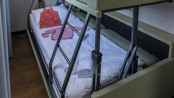 Ein Etagenbett mit ausziehbaren Bettkasten, einem weißen Kopfkissen, einem roten Handtuch und einem Paar rosafarbener Socken auf dem unteren Bett.
