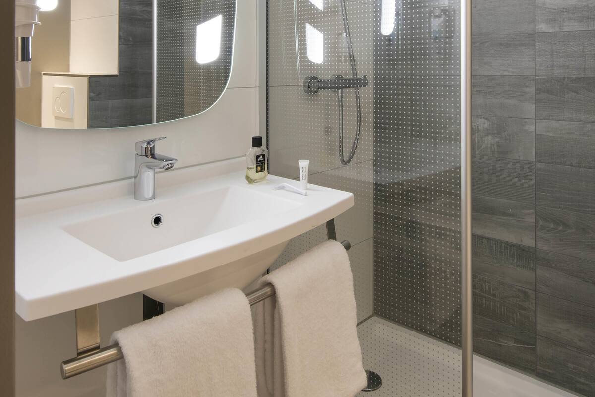 Un baño moderno con un lavamanos blanco, un espejo y una cabina de ducha con mampara de vidrio.
