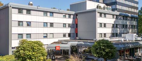 A modern hotel with a central entrance, outdoor seating area, and a parking lot.