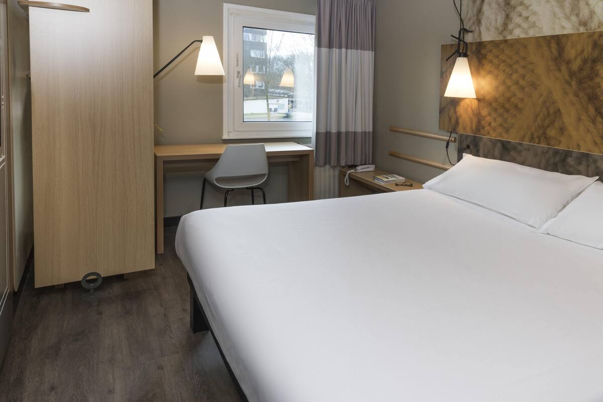 A hotel room with a bed, desk, chair, and a window with curtains.