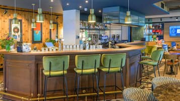 Zona de bar con mostrador, taburetes y un área de estar con sillas estampadas.