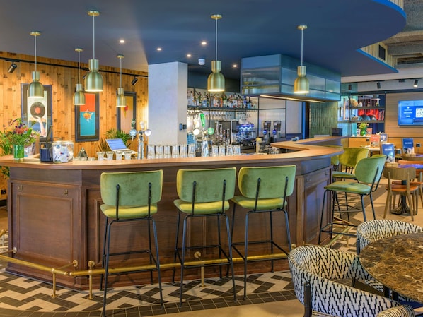 Zona de bar con mostrador, taburetes y un área de estar con sillas estampadas.