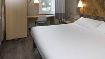 Una habitación de hotel con cama, escritorio, silla y ventana con cortinas.
