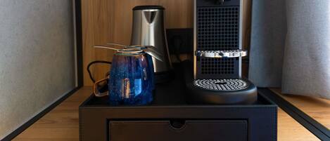 A compact coffee maker with a kettle and a mug on a wooden surface.