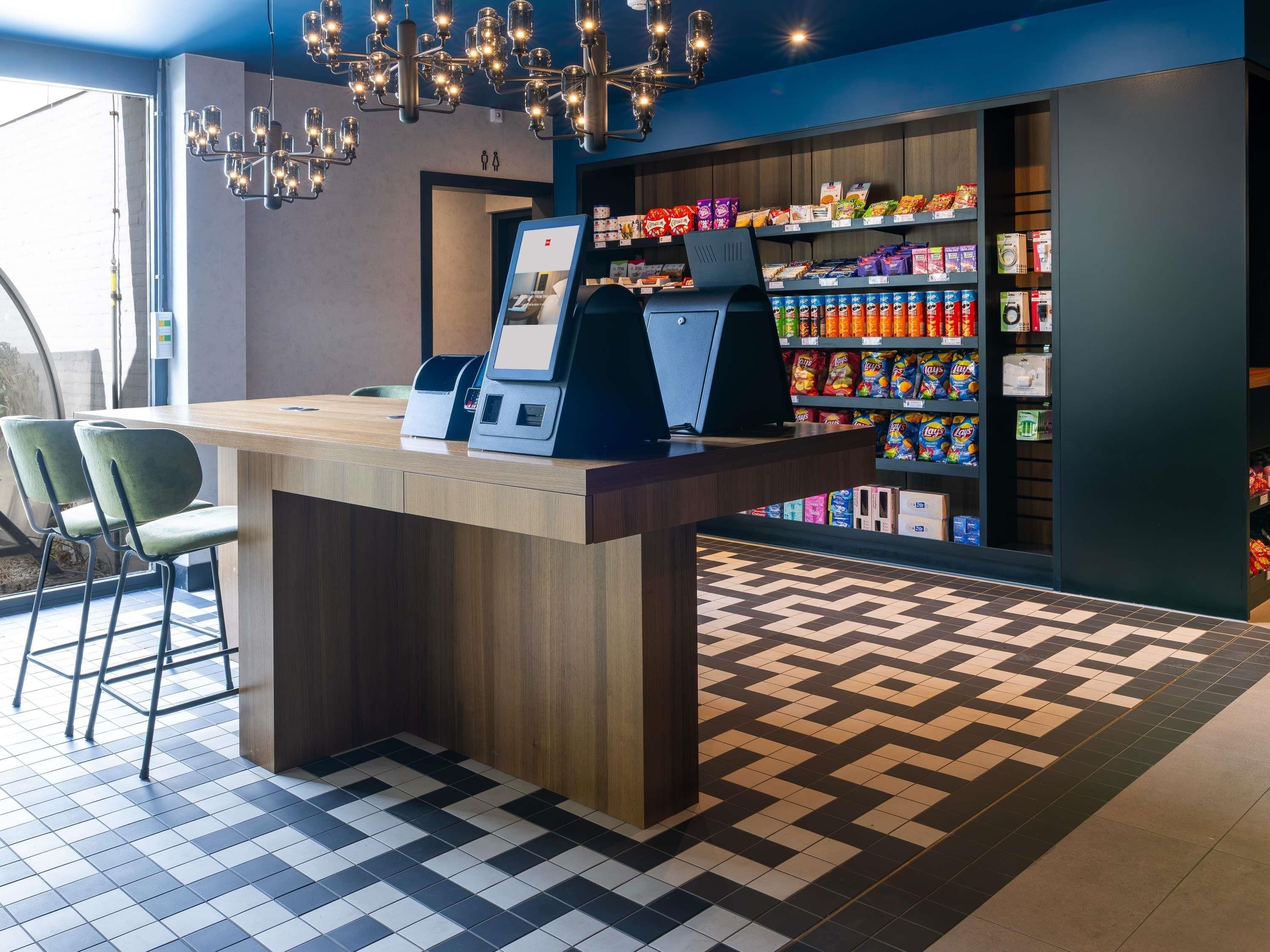 Un quiosco autoservicio con una pantalla digital, rodeado de estantes con aperitivos y un piso con diseño.