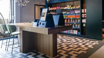 Un quiosco autoservicio con una pantalla digital, rodeado de estantes con aperitivos y un piso con diseño.