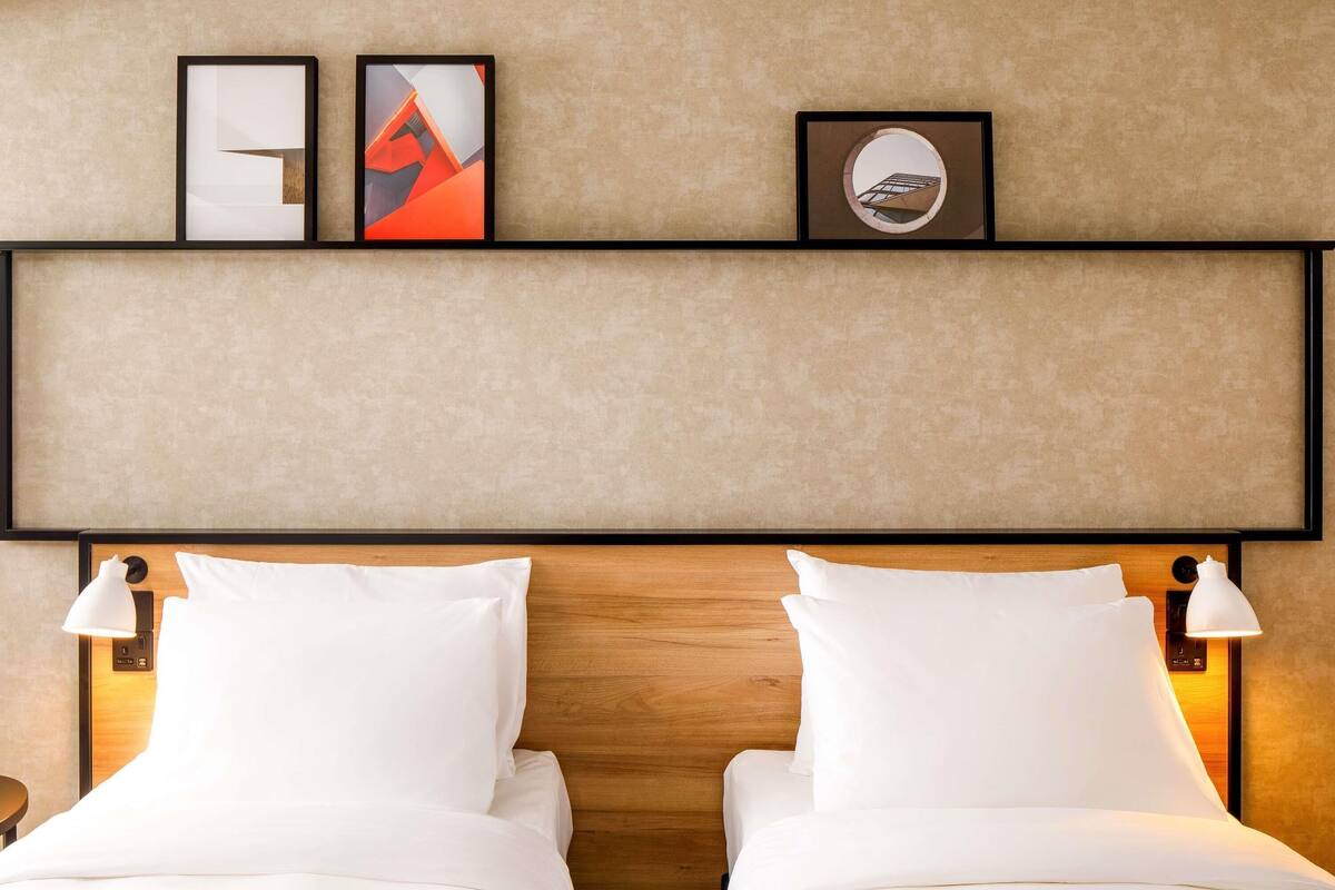 A hotel room with two beds, a wooden headboard, wall-mounted artwork, and bedside lamps.