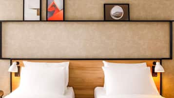 Habitación de hotel con dos camas, cabecera de madera, obras de arte en la pared y lámparas de noche.