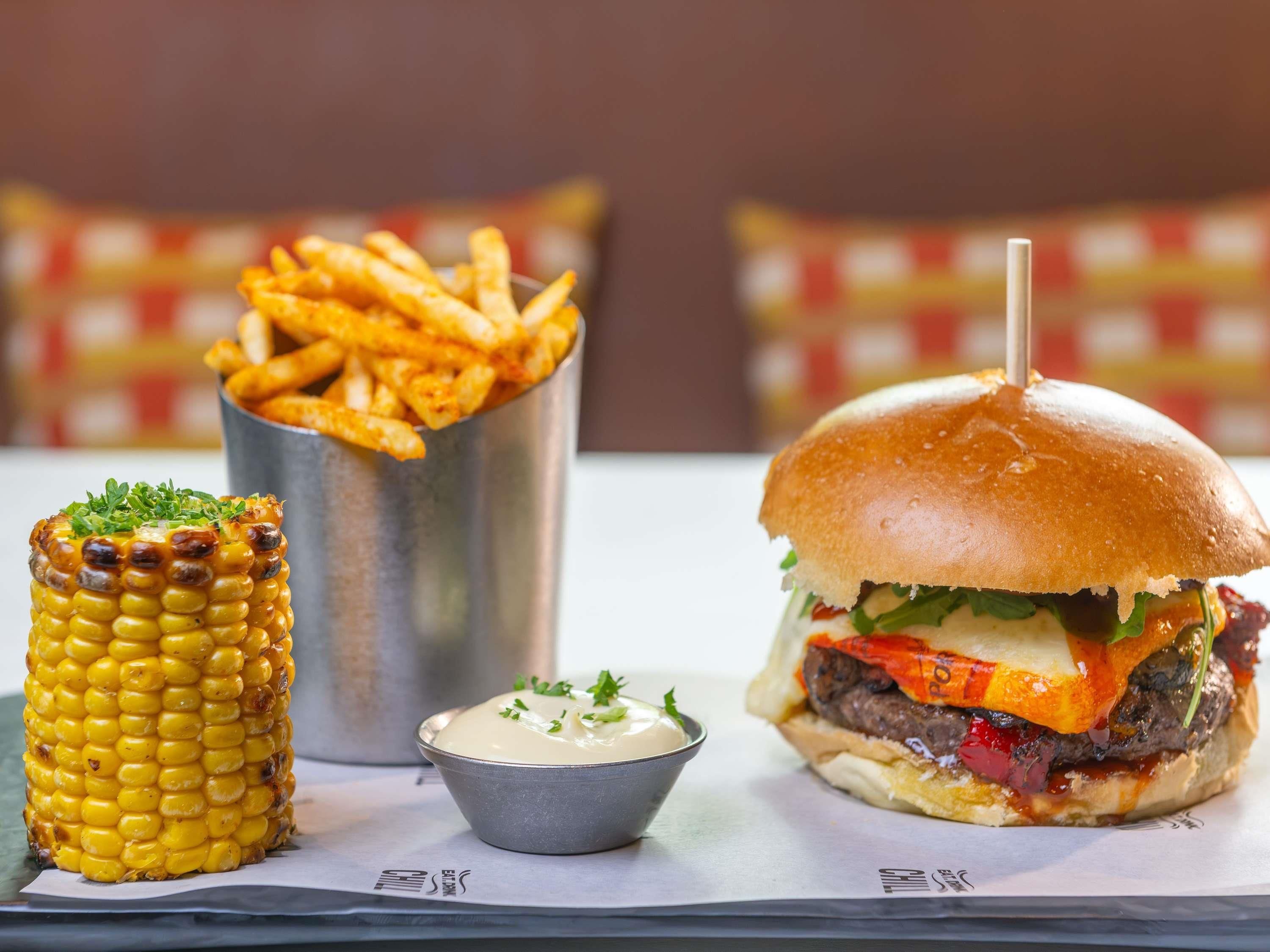 Una comida que incluye una hamburguesa, mazorca de maíz y papas fritas.