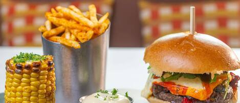 Una comida que incluye una hamburguesa, mazorca de maíz y papas fritas.