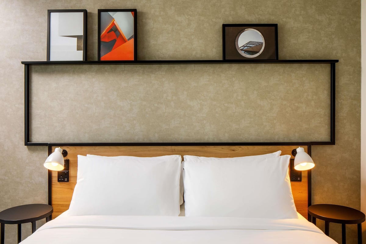 Habitación de hotel con una cama, dos mesitas de noche, un cabecero y una obra de arte colgada en la pared.