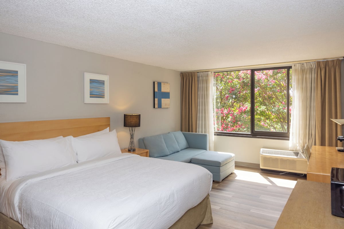 Ein Hotelzimmer mit einem großen Bett, einer Sitzecke, einem Schreibtisch und einem Fenster mit Vorhängen.
