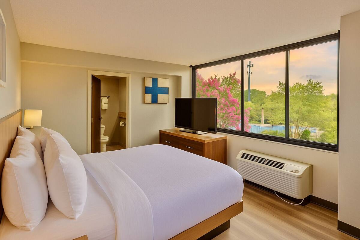 Ein Hotelzimmer mit Bett, Fernseher, Heizung und Fenster mit Blick auf Bäume und ein Gebäude.