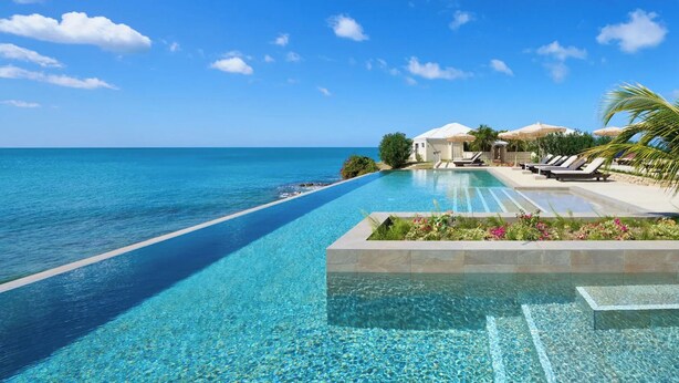 A clear blue pool with a view of the ocean, lounge chairs, and umbrellas. - Hawksbill Resort Antigua (St. John's)