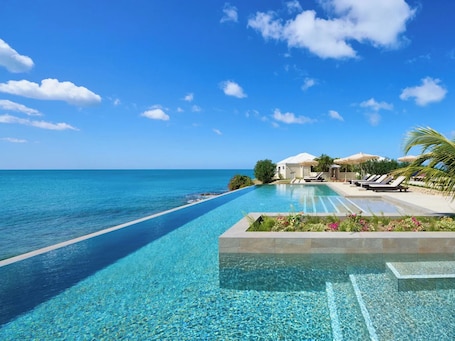 A clear blue pool with a view of the ocean, lounge chairs, and umbrellas.
