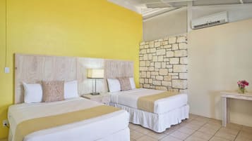 A hotel room with two beds, a stone wall, an air conditioning unit, and a small table with flowers.