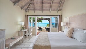 A bedroom with a bed, a desk, a chair, and a view of the beach. - Hawksbill Resort Antigua (St. John's)