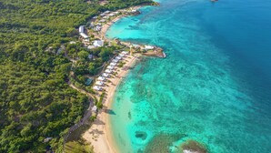An aerial view of a coastal resort with beach huts, a sandy shoreline, and clear turquoise waters. - Hawksbill Resort Antigua (St. John's)