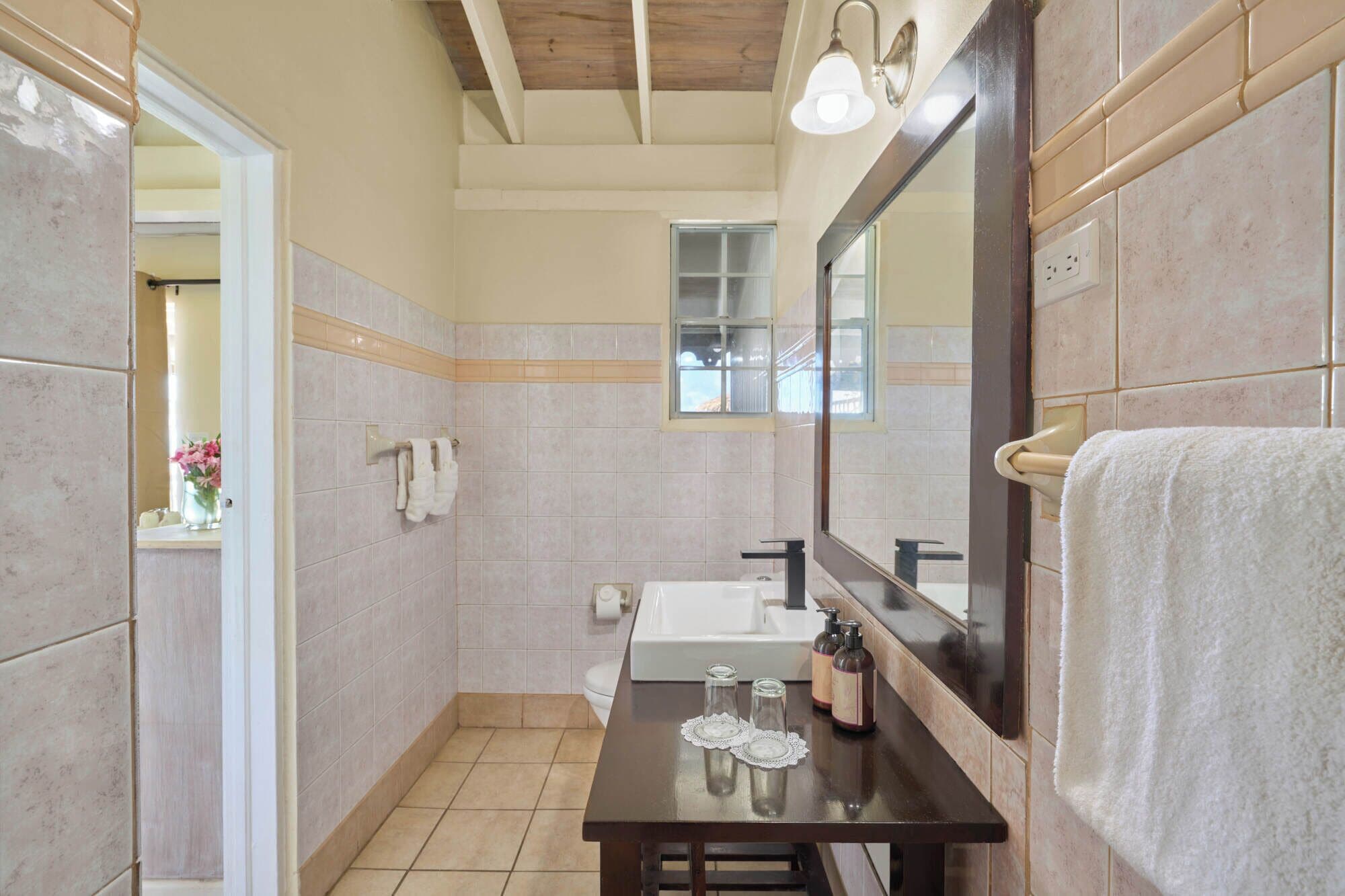 Een badkamer met een grote spiegel, een wastafel en een toilet. Handdoeken hangen aan de muur en boven de wastafel is een raam.