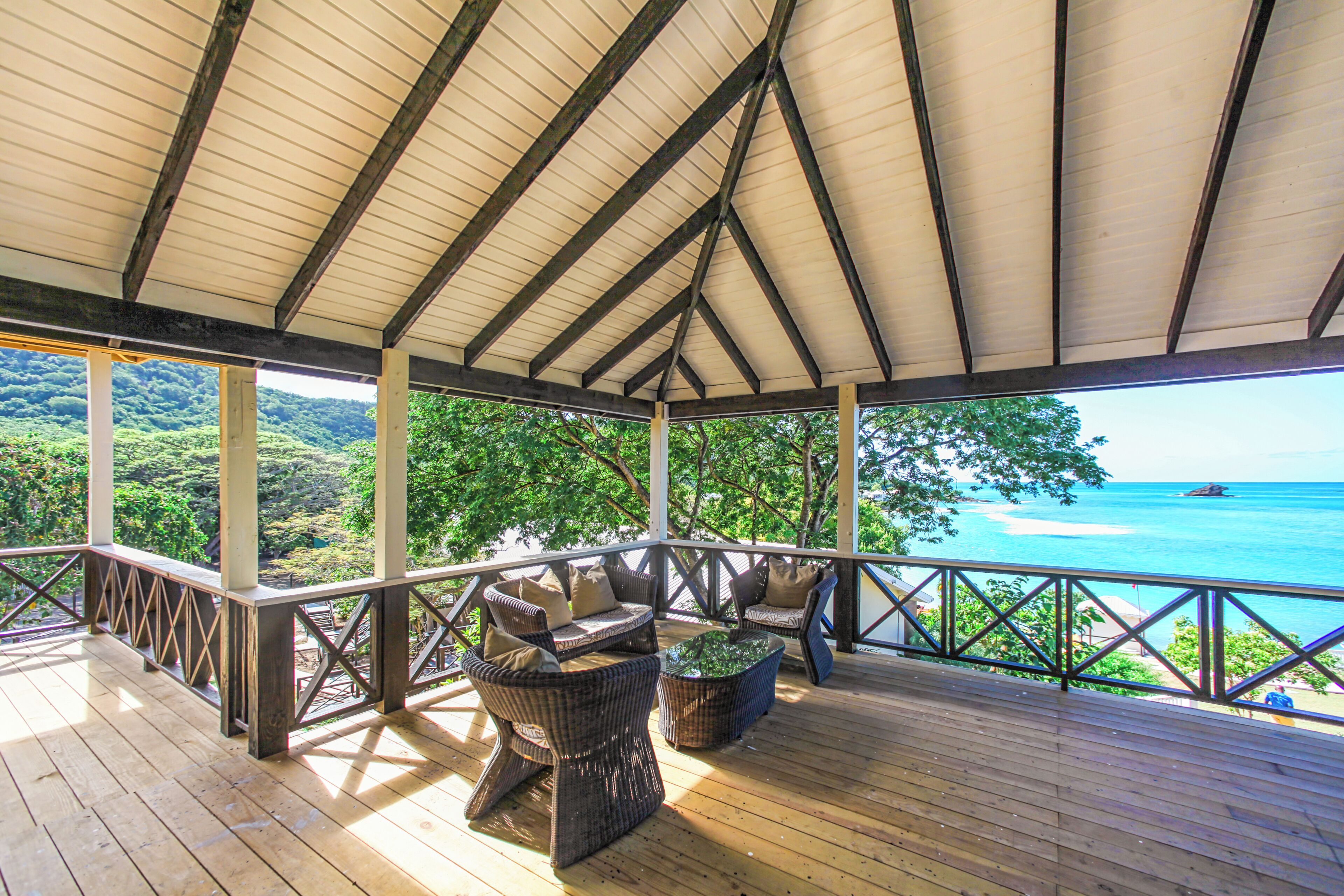 A covered outdoor seating area with wicker furniture and a view of the ocean.