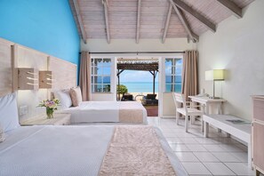 A hotel room with two beds, a desk, a chair, a small table, and a view of the beach. - Hawksbill Resort Antigua (St. John's)
