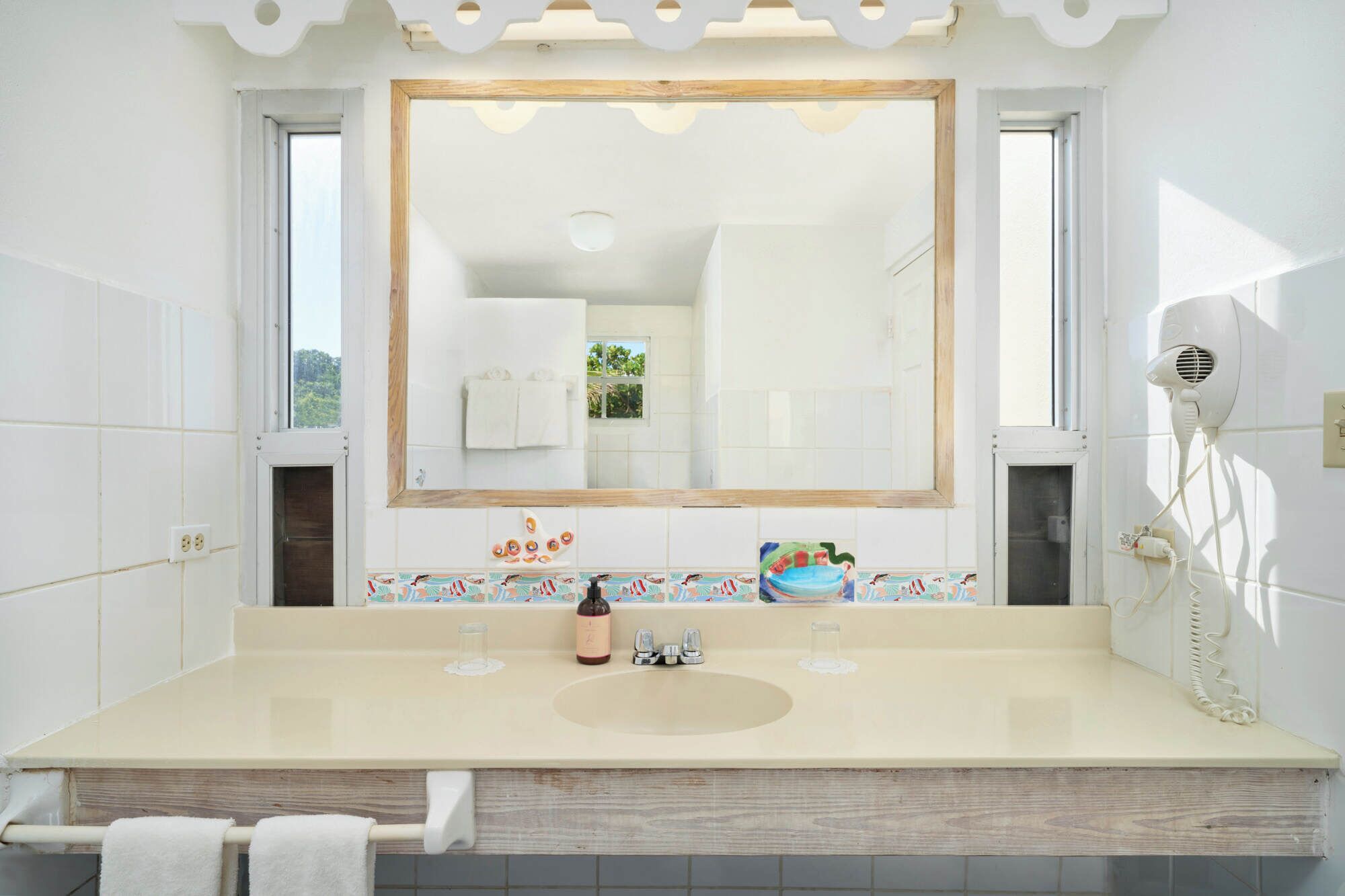 A bathroom with a large mirror, a sink, a hairdryer, and a window.