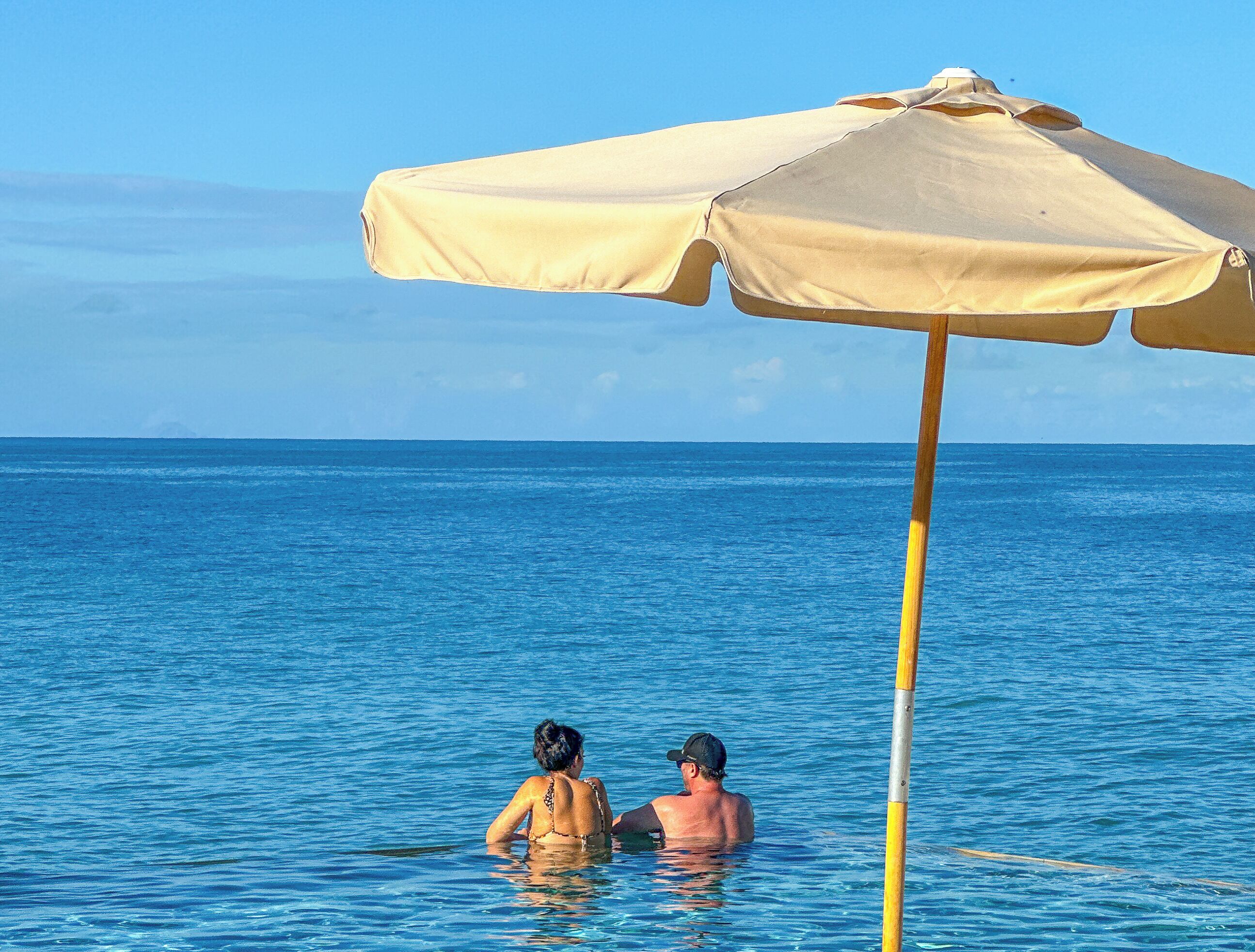 Deux personnes dans une piscine, avec un parasol de plage.