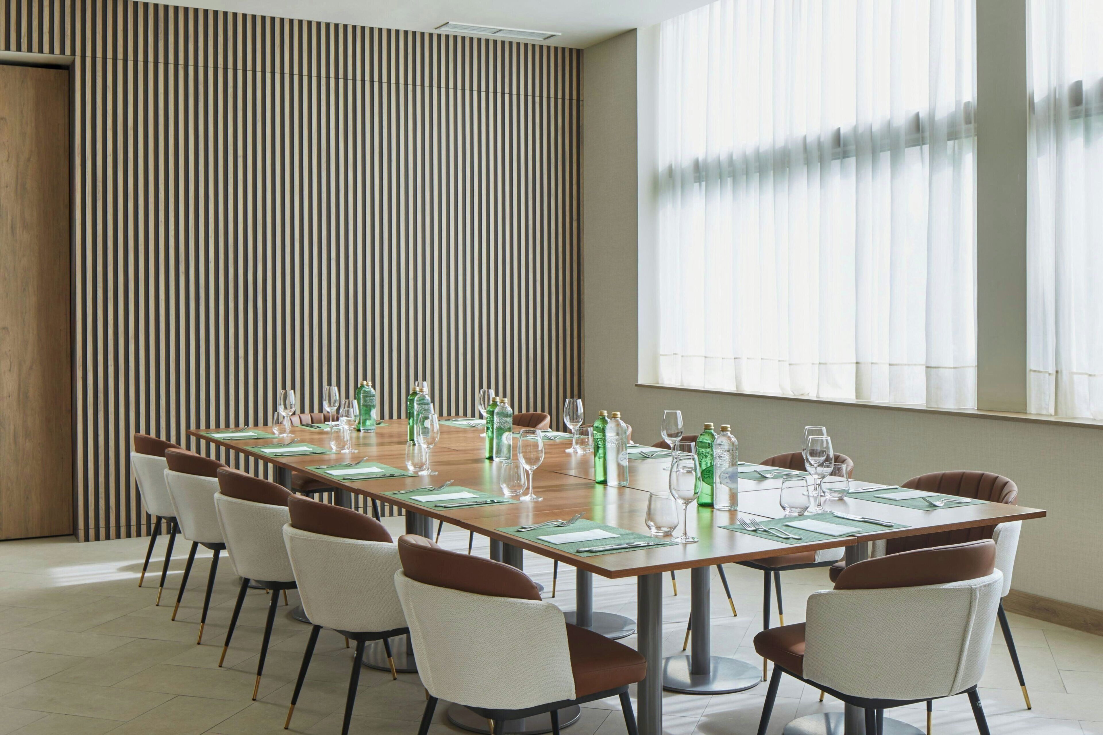 Uma sala de conferências com uma mesa comprida preparada para uma reunião, rodeada por cadeiras.