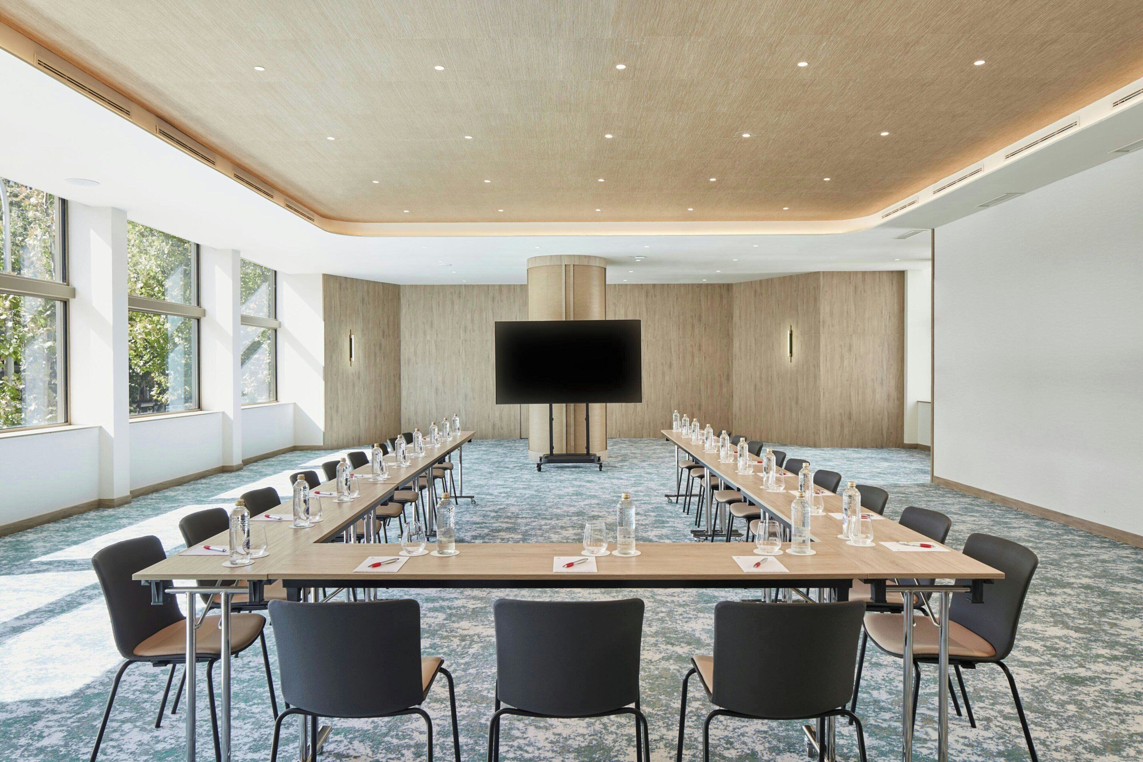 A conference room with a long table, chairs, a large screen, and windows.