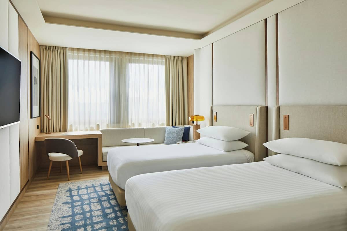 Une chambre d’hôtel avec deux lits, un bureau, une chaise et un téléviseur.