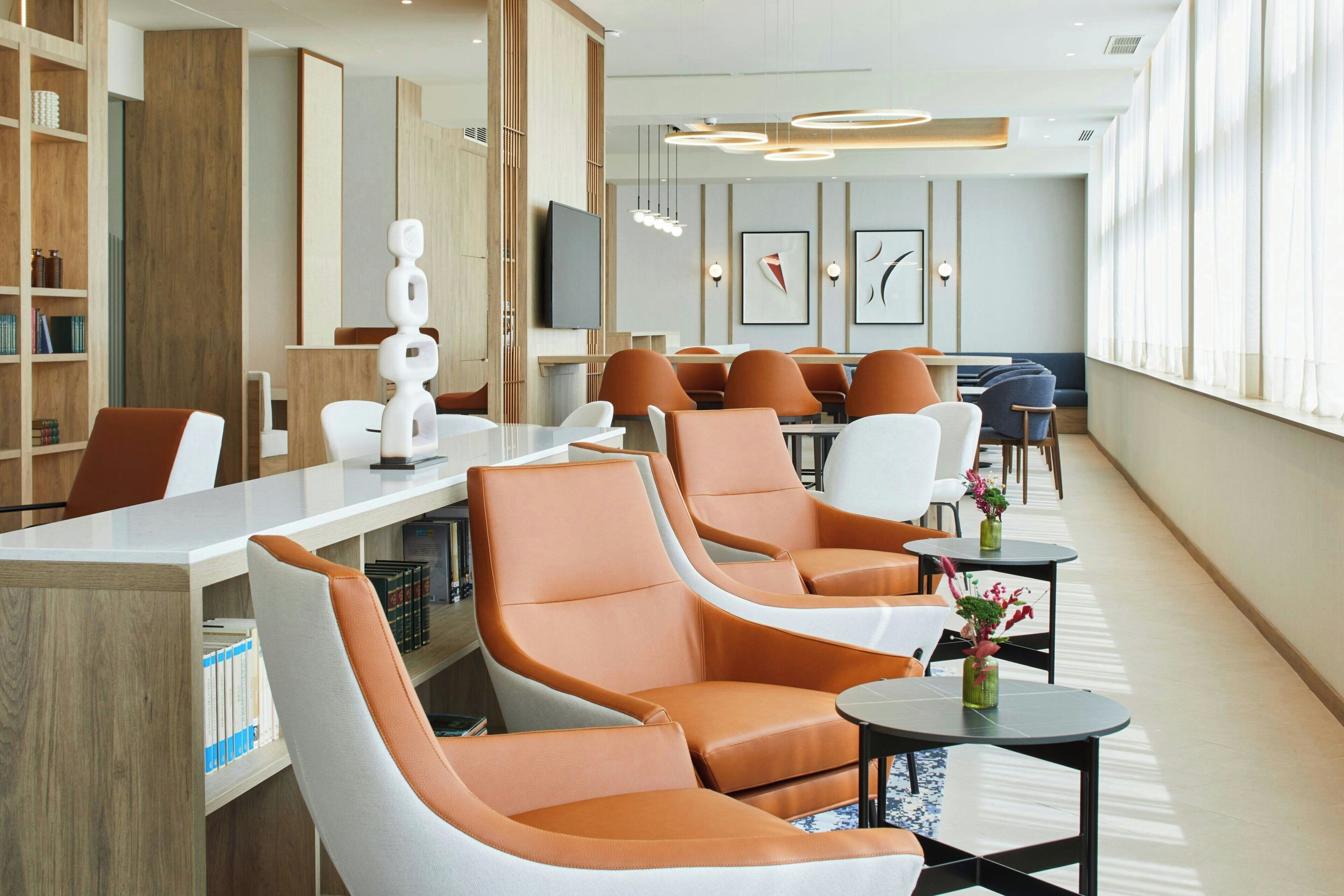 Um lobby moderno de hotel com poltronas de couro, balcão de recepção e uma grande janela que ilumina naturalmente o espaço.