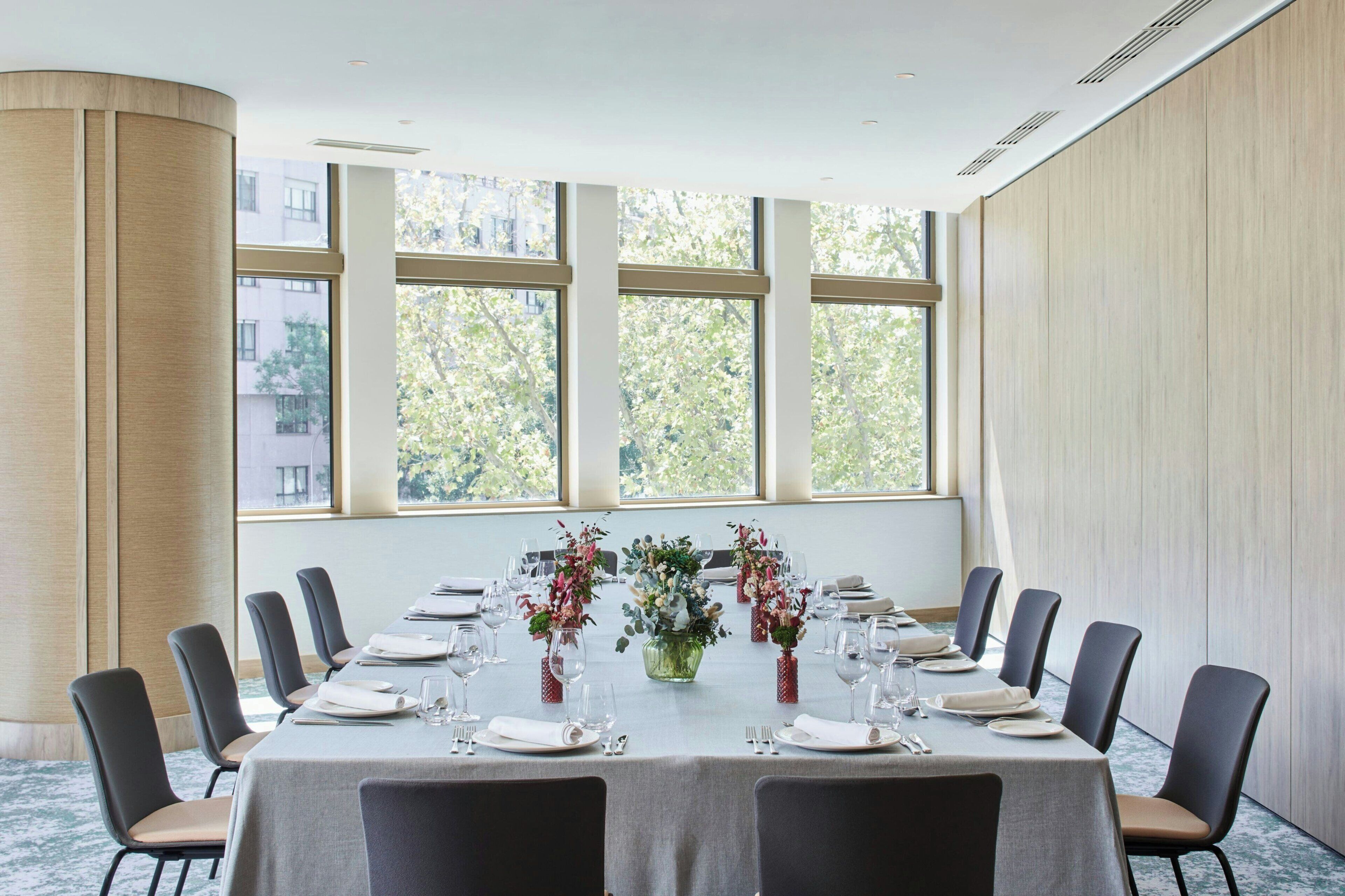 A conference room with a long table set for a meeting, large windows with a view of trees, and modern chairs.
