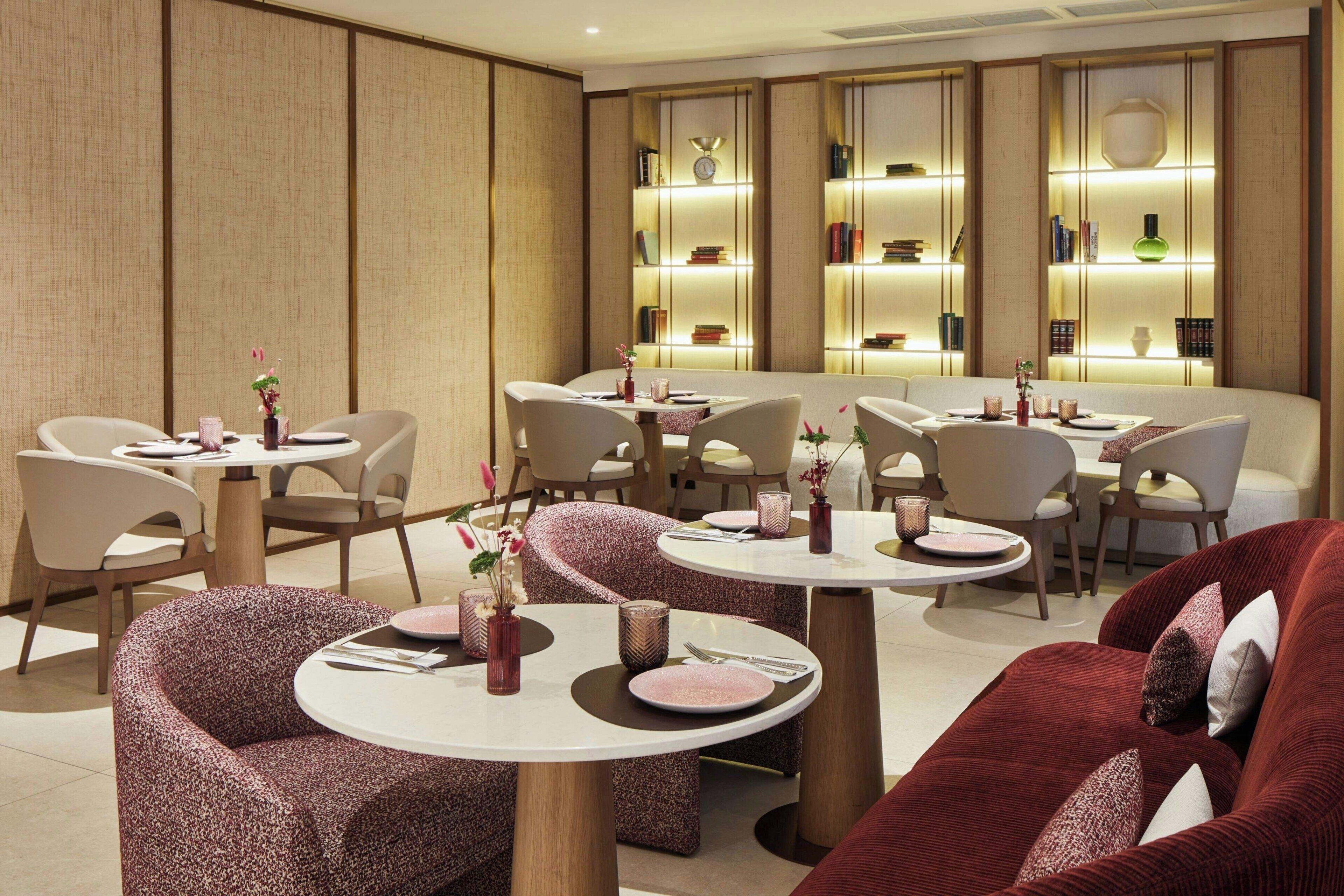 A modern dining area with round tables and cushioned chairs, featuring a warm color scheme and ambient lighting.
