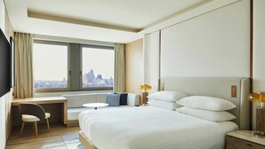 Habitación de hotel con una cama grande, un escritorio, una silla y vistas a la ciudad.