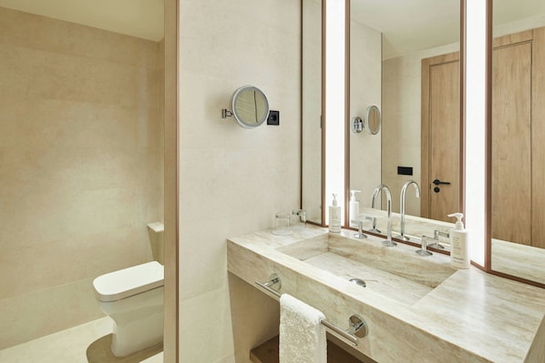 A modern bathroom with a dual sink, a toilet, a towel rack, and a large mirror.