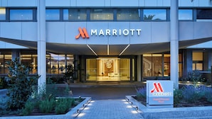 Entrada moderna de un hotel Marriott con fachada de vidrio, un vestíbulo bien iluminado y un cartel que indica que es el establecimiento Madrid Princess Plaza.
