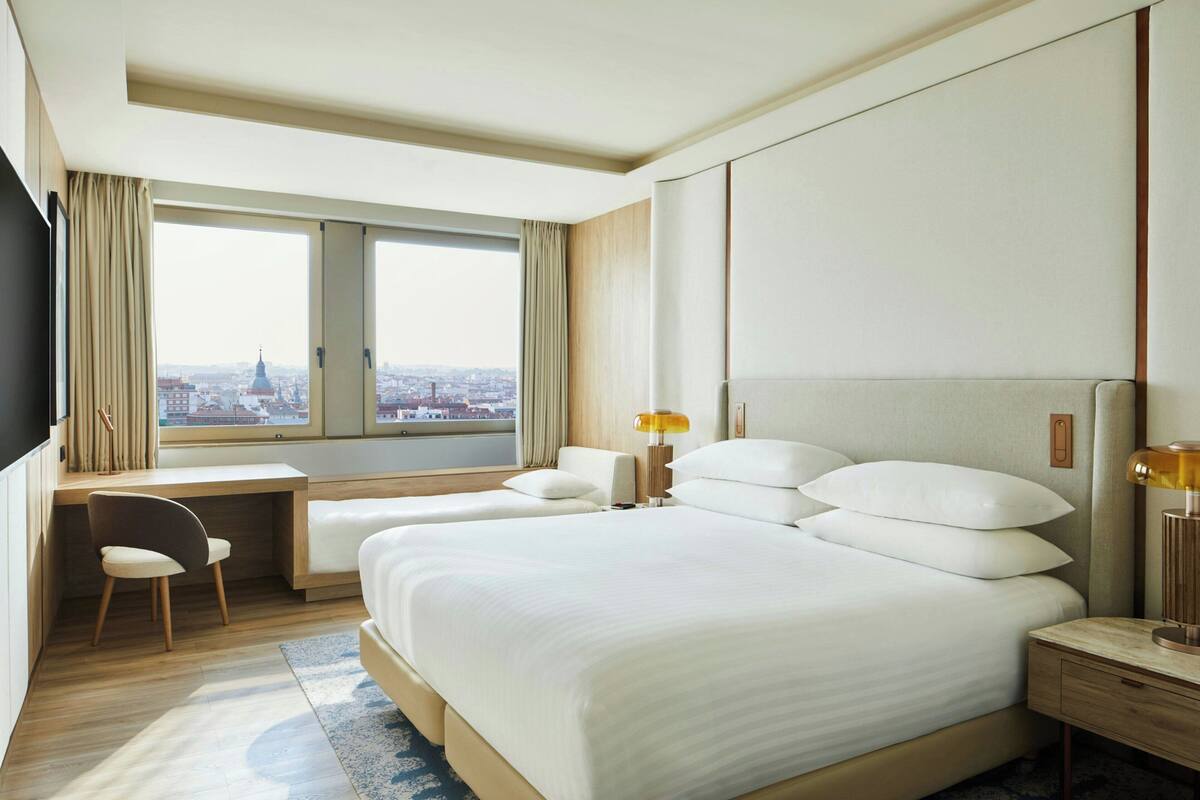 Une chambre d’hôtel avec un grand lit, un bureau et une chaise. Il y a une fenêtre donnant sur la ville.