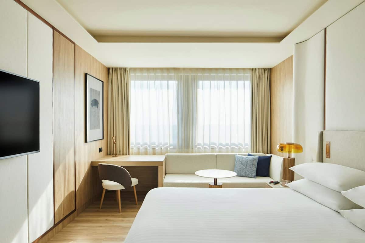 Une chambre d’hôtel avec un lit, un bureau, une chaise, une petite table ronde, un téléviseur et une lampe.