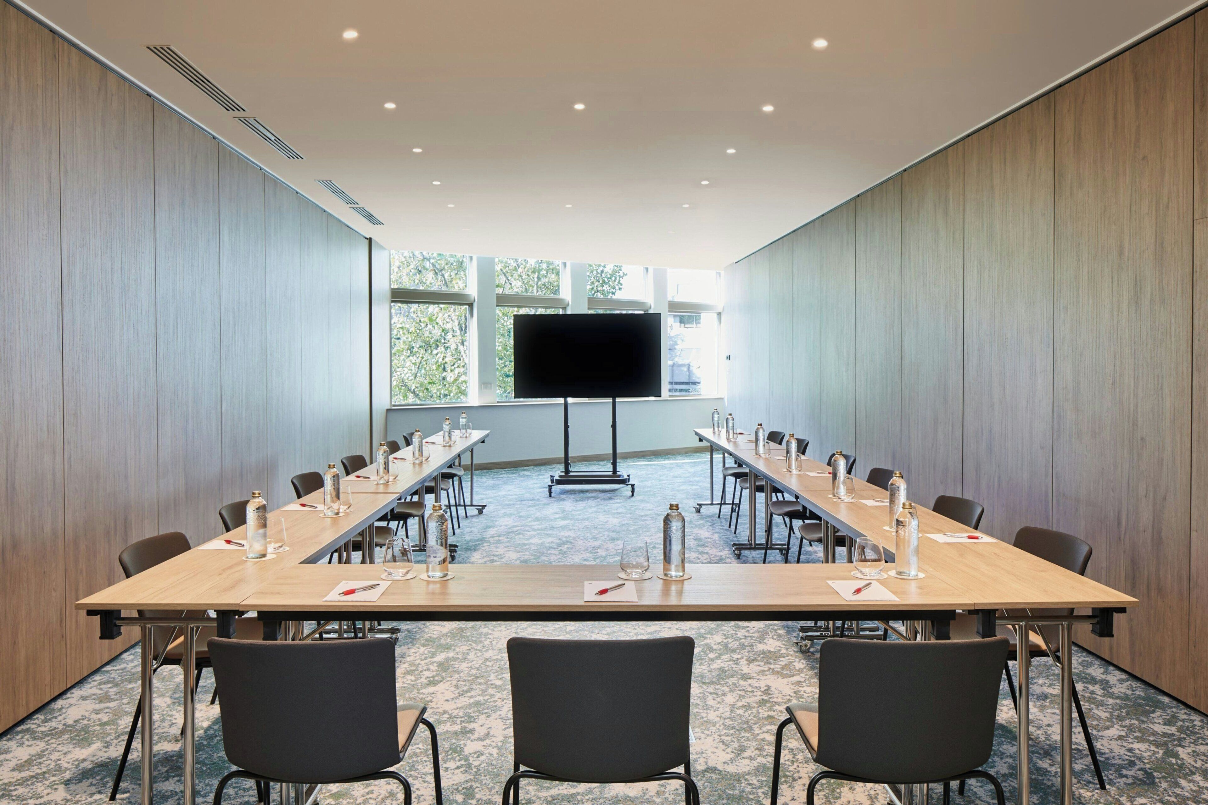 A conference room with a long table, chairs, a TV screen, and a projector stand.